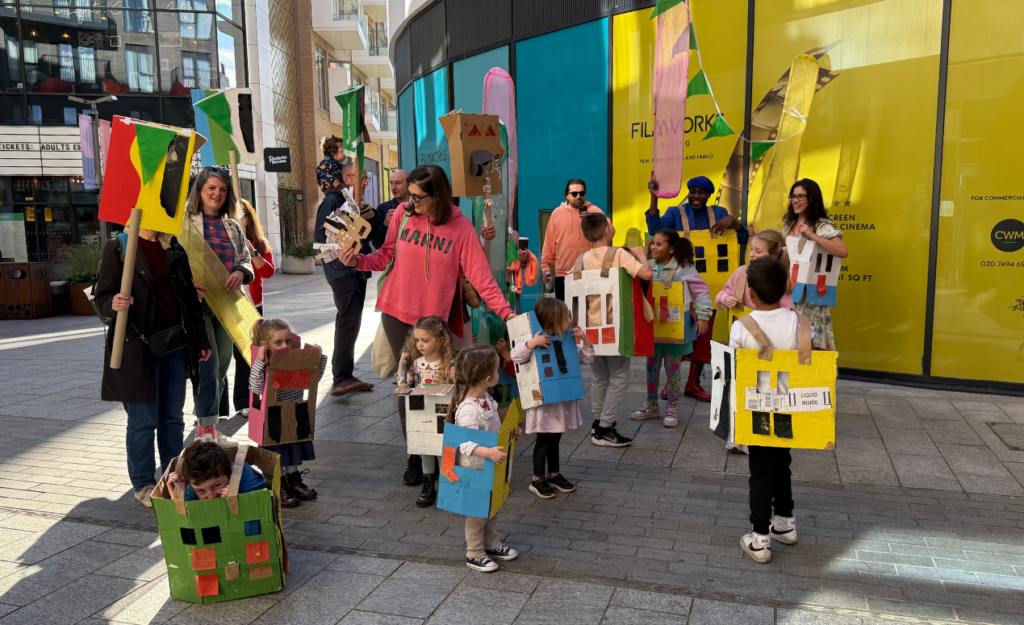 Children and families parade in colorful handmade costumes, celebrating creativity and community spirit at a Pitzhanger event.